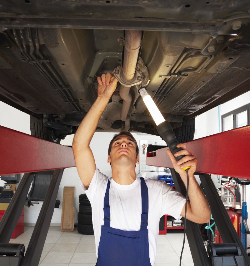 Mechanic standing under car engine and holding a lamp - MOT Testing Prudhoe